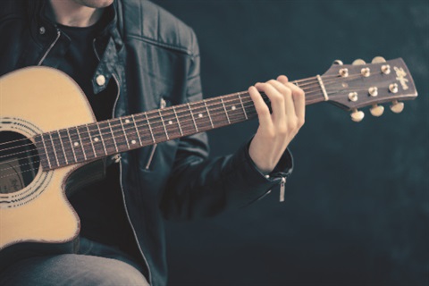 Man in leather jacket holding an acoustic guitar.